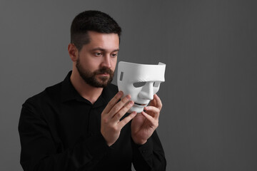 Multiple personality concept. Man putting on mask against grey background. Space for text