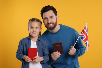 Immigration. Happy man with his daughter holding passports and flag of United Kingdom on orange...