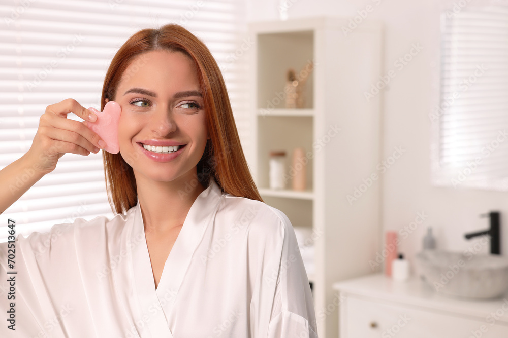 Sticker Young woman massaging her face with rose quartz gua sha tool in bathroom, space for text