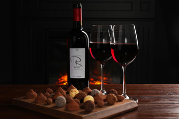 Red wine and chocolate truffles on wooden table against fireplace