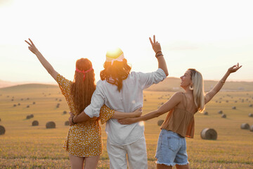 Hippie friends showing peace signs in field, back view