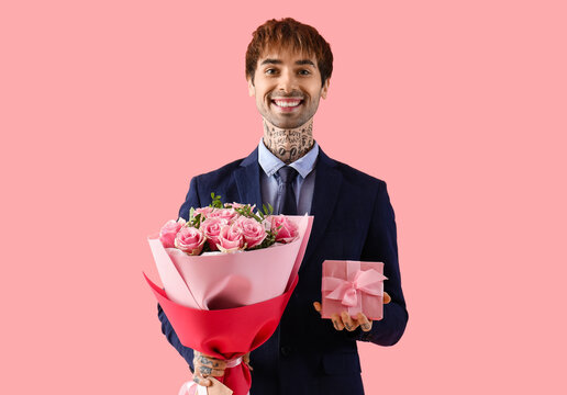 Handsome young man with bouquet of roses and gift for Valentine's day on pink background
