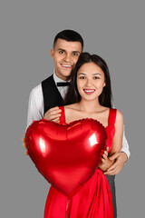 Fototapeta na wymiar Young couple with heart-shaped air balloon for Valentine's day on grey background