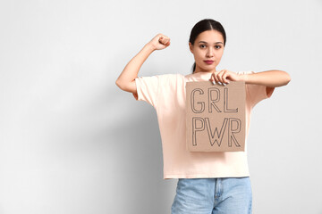 Young woman with sign GRL PWR flexing muscles on white background. Feminism concept