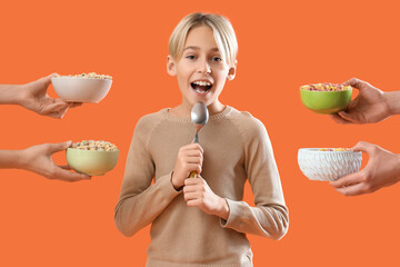 Cute little boy holding spoon and hands with cereal rings on orange background