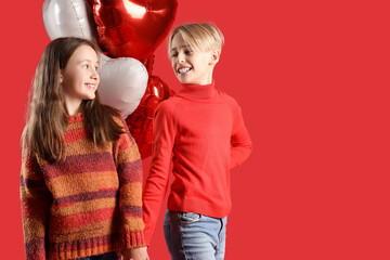 Happy little children with heart-shaped air balloons holding hands on red background. Valentine's day celebration