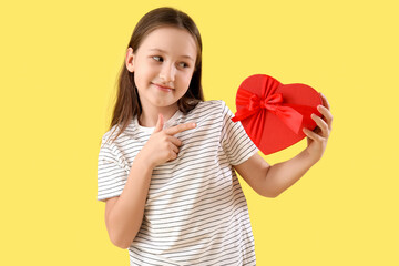 Cute little girl pointing at gift for Valentine's day on yellow background