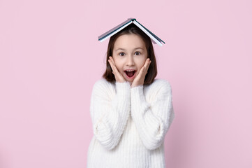 Surprised little girl with book on pink background