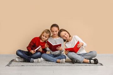 Little children reading books while sitting on floor near beige wall