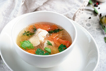 Chicken broth with vegetables and herbs in a white bowl. Transparent soup with homemade chicken.