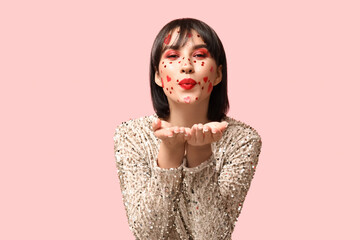 Beautiful young young woman with creative makeup for Valentines Day blowing kiss on pink background