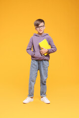 Cute schoolboy in glasses holding books on orange background - obrazy, fototapety, plakaty