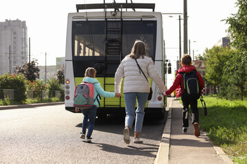 Fototapeta premium Being late for school. Senior woman and her grandchildren with backpacks running towards bus outdoors, back view