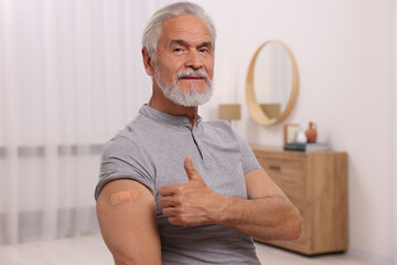 Senior man with adhesive bandage on his arm after vaccination showing thumb up at home