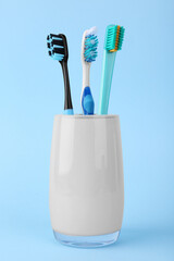 Different toothbrushes in holder on light blue background