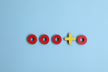 Choice concept. Red wooden circles and yellow cross on light blue background, flat lay