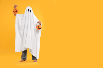 Woman in white ghost costume holding pumpkin buckets on yellow background, space for text. Halloween celebration - obrazy, fototapety, plakaty