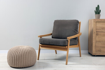 Comfortable armchair, chest of drawers and pouf near light grey wall indoors. Interior design