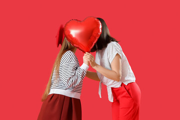 Young lesbian couple kissing behind balloon on red background. Valentine's Day celebration