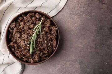 Fried ground meat in bowl and rosemary on brown textured table, top view. Space for text