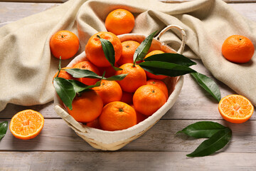 Wicker basket with sweet mandarins and leaves on grey wooden background