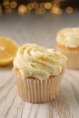 Tasty cupcake with cream and lemon zest on white wooden table, closeup