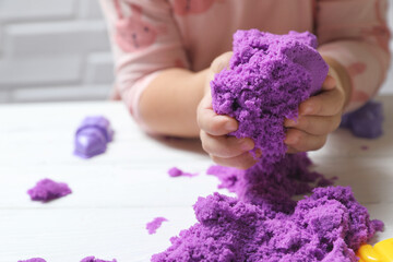 Little child playing with kinetic sand at white table, closeup - obrazy, fototapety, plakaty