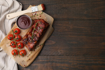 Tasty roasted pork ribs served with sauce and tomatoes on wooden table, top view. Space for text