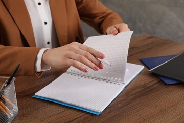 Woman taking notes at wooden table indoors, closeup