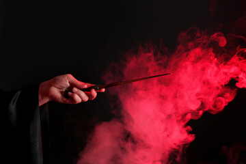 Magician holding wand in smoke on dark background, closeup - obrazy, fototapety, plakaty