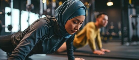 Asian Muslim woman exercising with partner at the gym in a plank position - obrazy, fototapety, plakaty