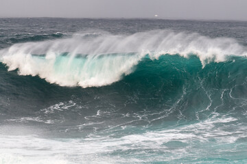 An angry turquoise green colour massive rip curl of a wave as it rolls along a beach. The white...