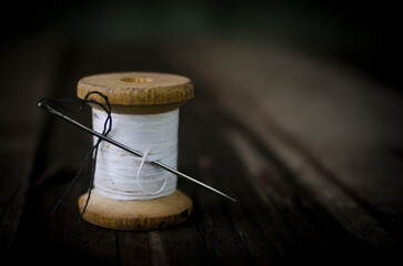 a bobbin with white thread and a needle with black thread stuck into it stands on a wooden table. closeup thread for sewing and needlework, old reel of thread