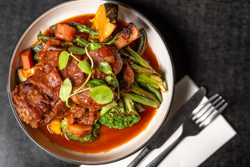 Roasted lamb shank with grilled pumpkin and green vegetables in a round white bowl