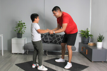 Latino dad and son prepare to exercise in their living room to lose weight, avoid obesity, and improve their family health