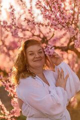 Fototapeta premium Woman blooming peach orchard. Against the backdrop of a picturesque peach orchard, a woman in a long white dress enjoys a peaceful walk in the park, surrounded by the beauty of nature.