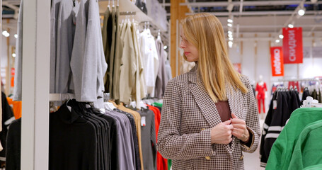 Naklejka na ściany i meble A young woman tries on a jacket in a clothing store