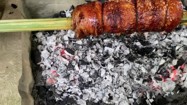 Grilling lechon belly in the traditional way. Whole piece of pork on a bamboo spit over coals. 