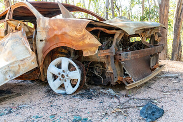Photograph of a small car that has been abandoned on a dirt road in a large forest and then set on...