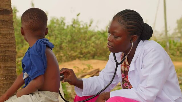 Africa healthcare: black female doctor listening the lungs of a young children using stethoscope in open air clinic hospital 
