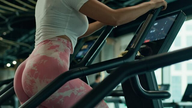 Asian girl trains her legs and glutes on a stepper at modern gym, low angle shot