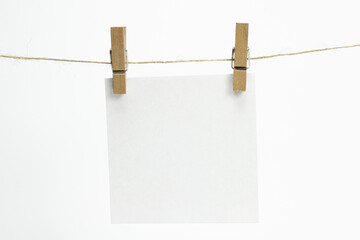 Single empty paper sheet for notes that hang on a rope with clothespins and isolated on white. Blank white cards on rope mockup template.