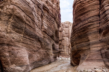 A small  shallow stream flows between high rocks with beautiful natural patterns on their walls along walking trail in Wadi Numeira gorge in Jordan