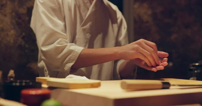 Hands, chef and brush for sushi, food or meal preparation on table for diner, cuisine or cooking in night. Person, kitchen or restaurant with soy sauce, ready and service for nutrition, diet or snack