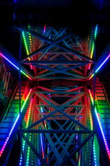 rainbow lights reflecting off the steel beams of a ferris wheel at night