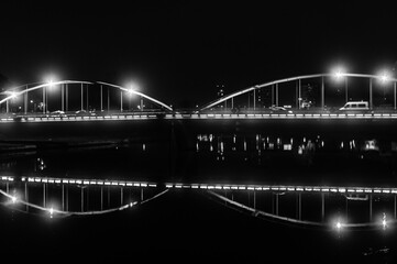 kontury oświetlonego mostu nad rzeką w nocy na fotografii czarno-białej