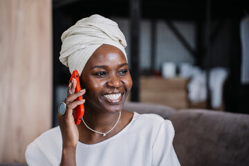 Woman in elegant white dress and headwrap smiles while using smartphone, radiating grace and...