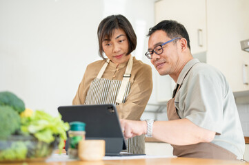 Obraz premium Lovely Asian couples are looking at an online recipe on a tablet and cooking in the kitchen together
