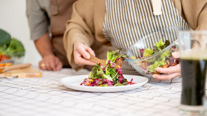 A lovely wife is serving a salad on a plate after cooking it with her husband in the kitchen.