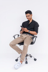 A young man chatting on his phone while sitting relaxed on his office armchair. Passing the time checking his social media. Isolated on a white backdrop.